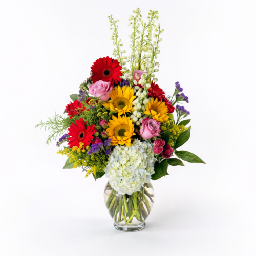 A Colorful Medley, a glass vase brimming with fresh daisies, sunflowers, roses, and more, is artfully displayed against a white background—ideal for flower delivery in Clayton NC.