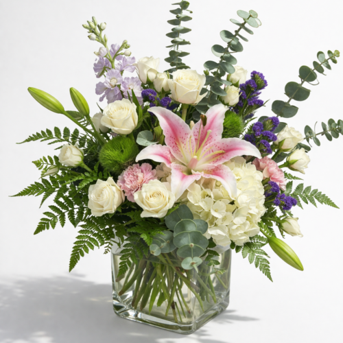 Softly Elegant Blooms: A glass vase arranged with a mixed bouquet—pink lily, white roses, hydrangeas, purple accents, and eucalyptus—by The Florist at Plantation in Clayton. Displayed against a plain white background.
