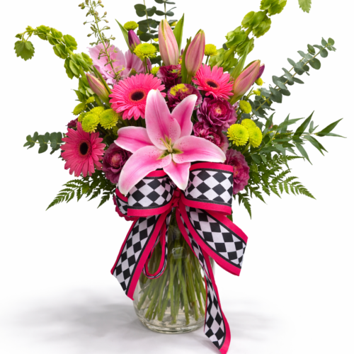The Pink Showstopper features pink lilies, gerbera daisies, and lush greenery in a glass vase, accented with a black-and-white checkered ribbon edged in pink—a stunning arrangement from your trusted Clayton NC florist.