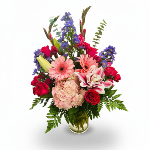 Bright Harmony Vase: A vibrant floral arrangement in a clear glass vase with pink gerbera daisies, lilies, blush hydrangeas, red roses, purple blooms, and greenery. Perfect for any occasion with reliable Flower Delivery in Clayton NC.