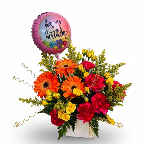 Birthday Sparkle Celebration: A vibrant mix of orange, red, and yellow blooms in a white vase with gold spirals and a pink Happy Birthday balloon from The Florist at Plantation—Clayton NC’s trusted florist for special occasions.