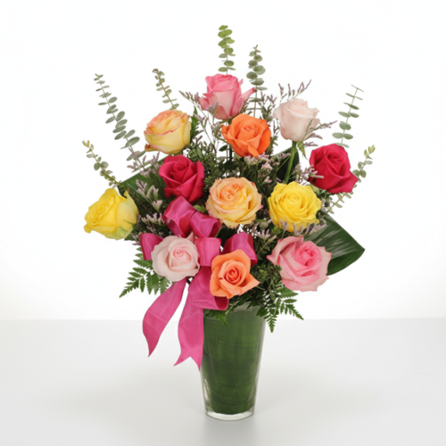 Colorful Rose Madness by The Florist at Plantation features a glass vase filled with assorted pink, yellow, orange, and red roses, accented with greenery and eucalyptus, and finished with a pink ribbon. Arrangement is displayed on a white background.