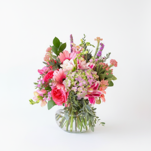 Floral Daydream—an artful arrangement of pink roses, gerbera daisies, purple blooms, and lush greenery in a clear glass vase—handcrafted by your Clayton florist. Perfect for brightening any space with vibrant color.