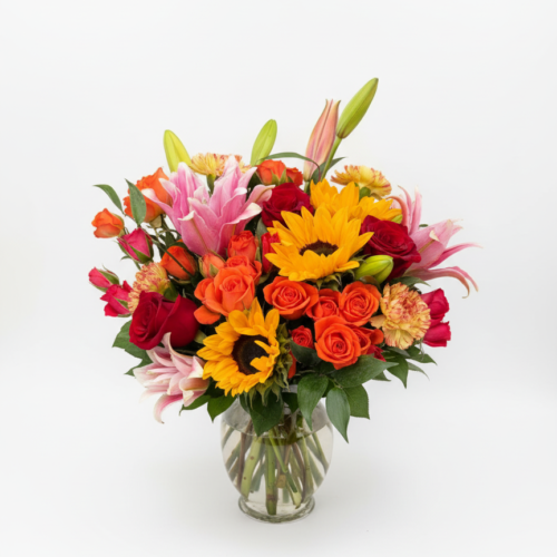 The Golden Ember Bouquet features sunflowers, pink lilies, red and orange roses, and assorted greenery in a clear glass vase—artfully arranged by The Florist at Plantation, your trusted Clayton NC florist.