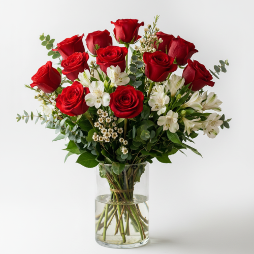 A clear glass vase filled with a bouquet of red roses, white alstroemeria, small white filler flowers, and green foliage, set against a plain white background.